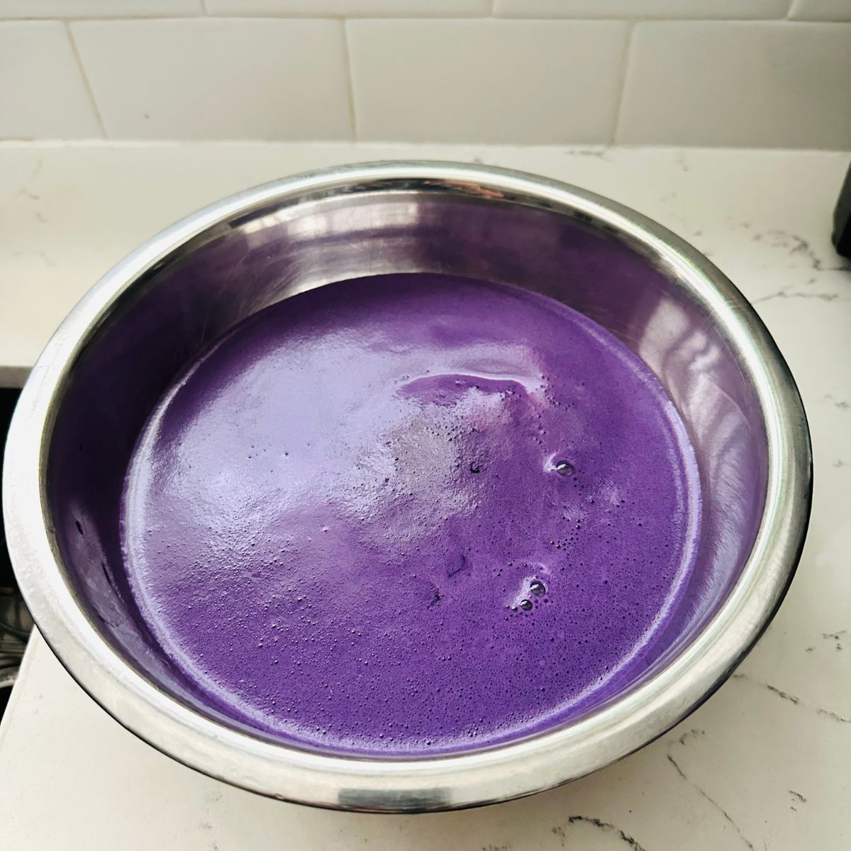 Straining the purple custard mixture through a fine mesh sieve into a bowl to remove lumps