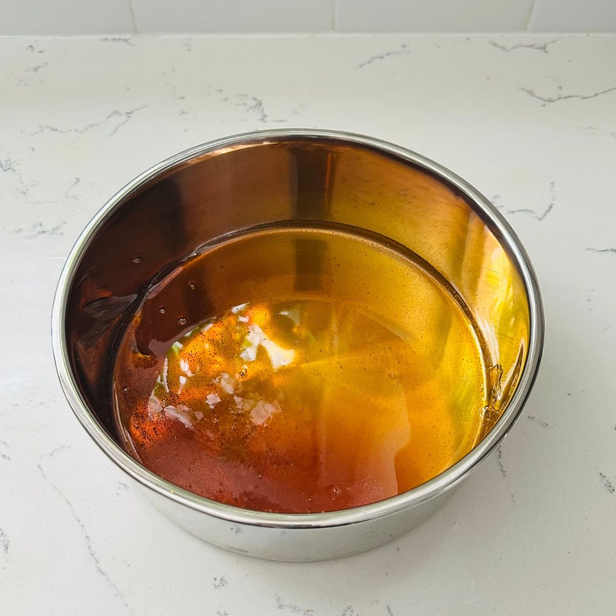 Caramel coating the bottom of an 8×8 round baking pan, ready for the ube leche flan custard.