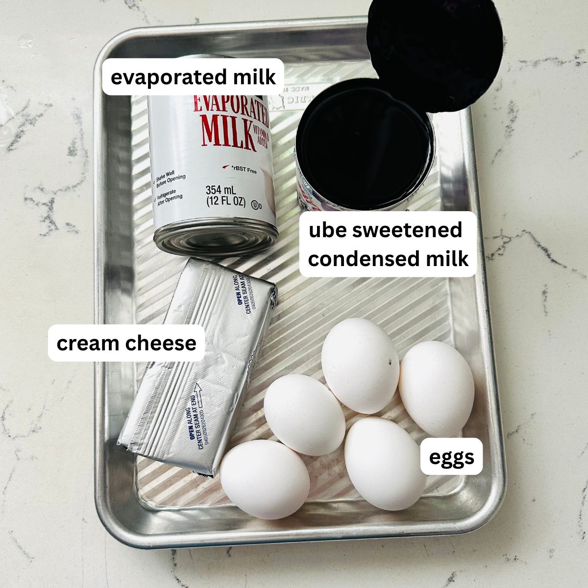 Ube leche flan ingredients laid out, showing the four main items: whole eggs, evaporated milk, ube condensed milk, and cream cheese.