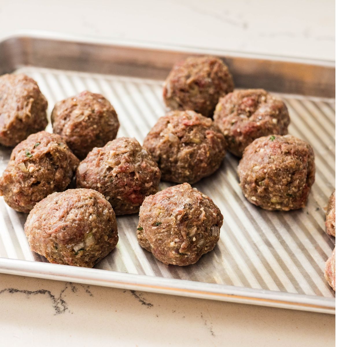 Raw beef meatballs formed into large balls on a tray.
