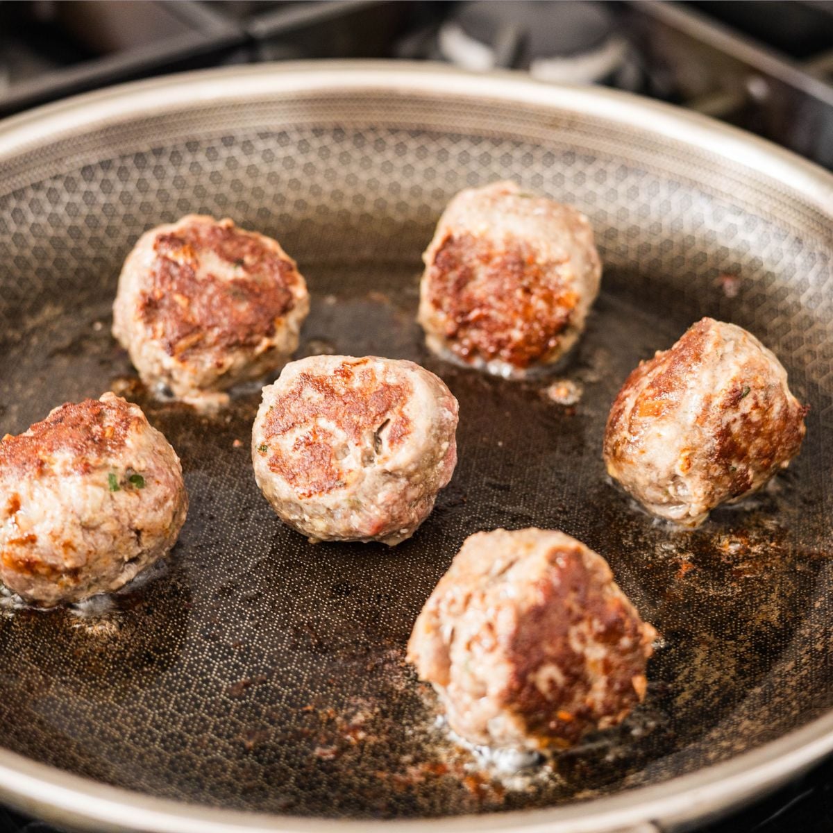beef meatballs browning in a skillet with golden crust on the outside