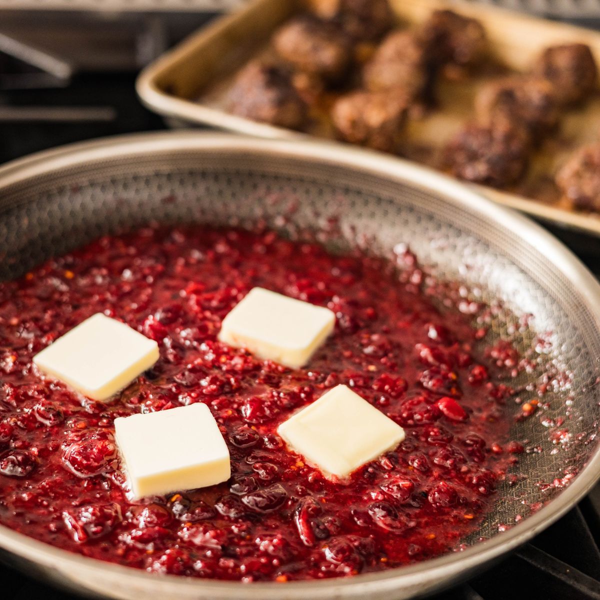 Homemade cranberry sauce simmering in a skillet pan topped with cold butter.
