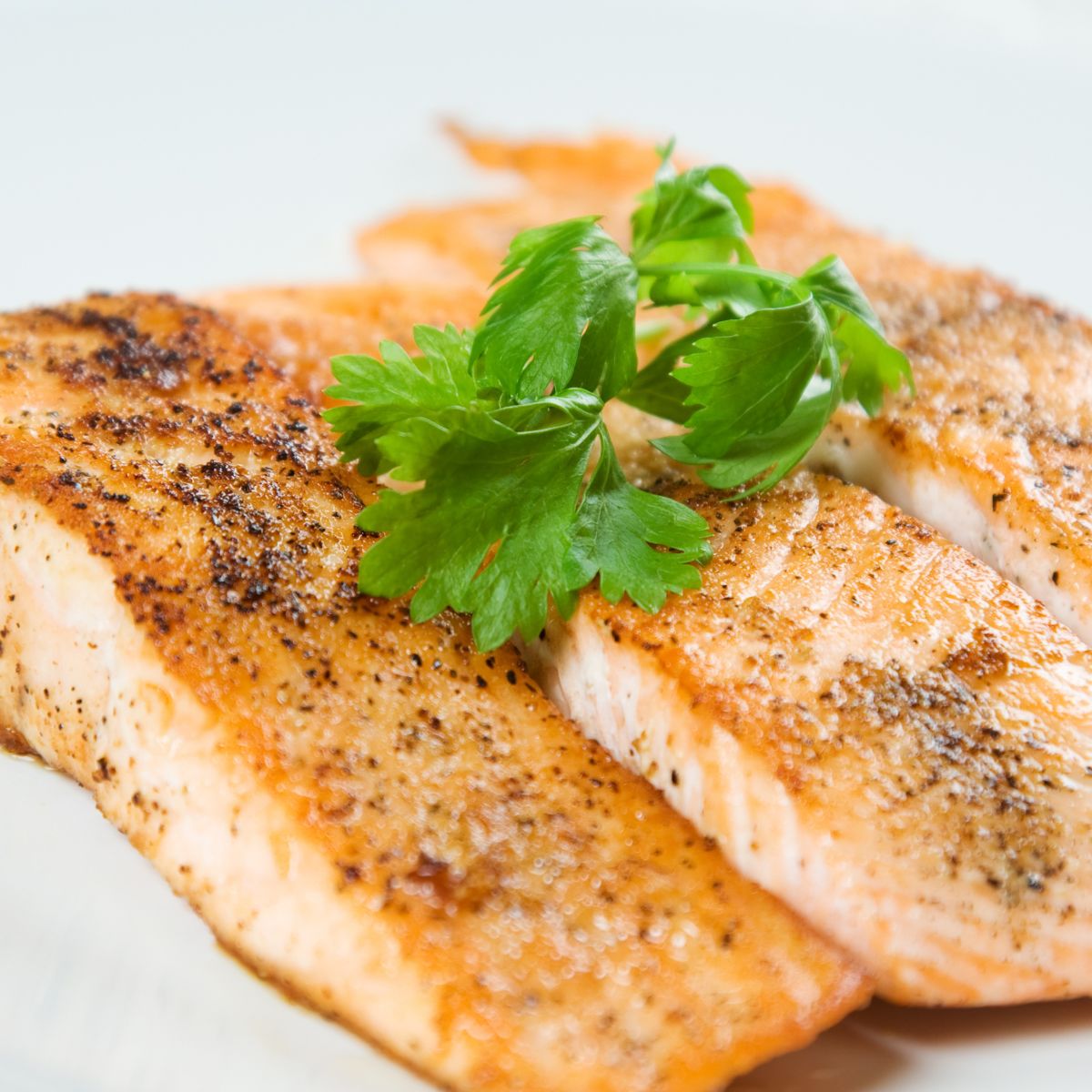 Baked salmon fillets with a golden-brown crust, seasoned with black pepper and garnished with fresh parsley.