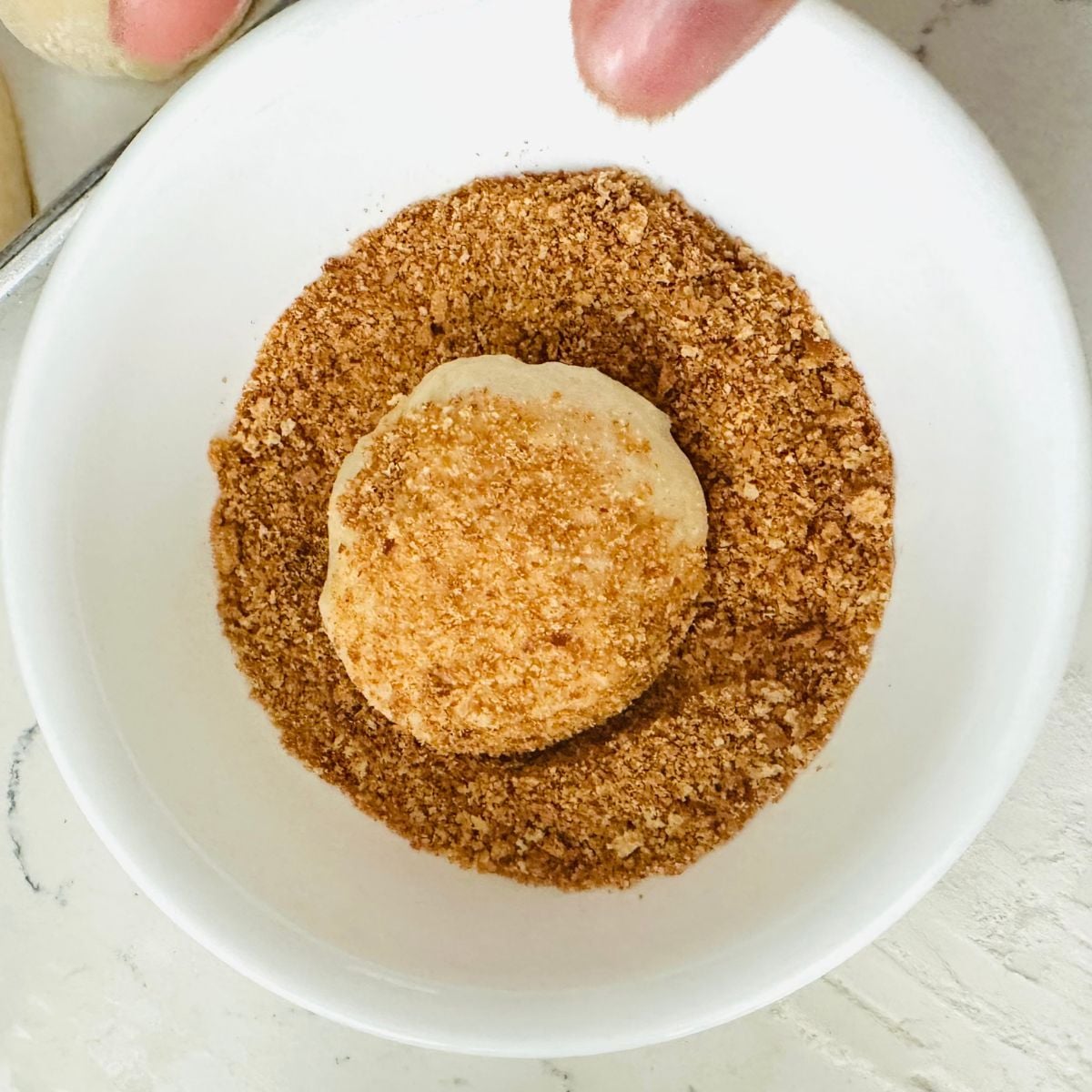 Pandesal dough ball being rolled in fine breadcrumbs before the second rise.