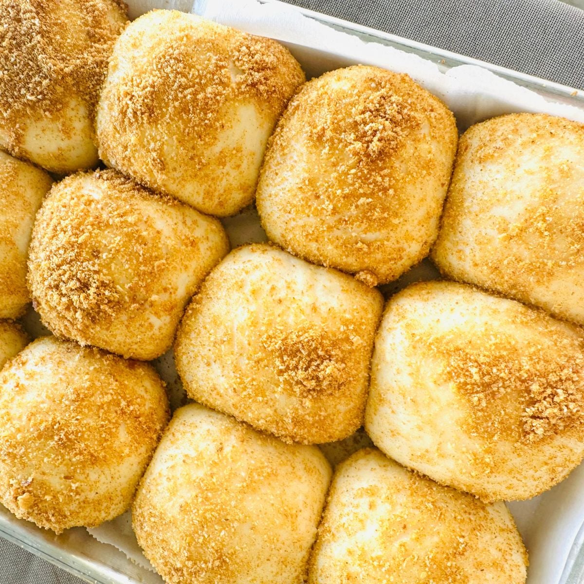 Tray of unbaked pandesal rolls coated with breadcrumbs and arranged closely together for baking.
