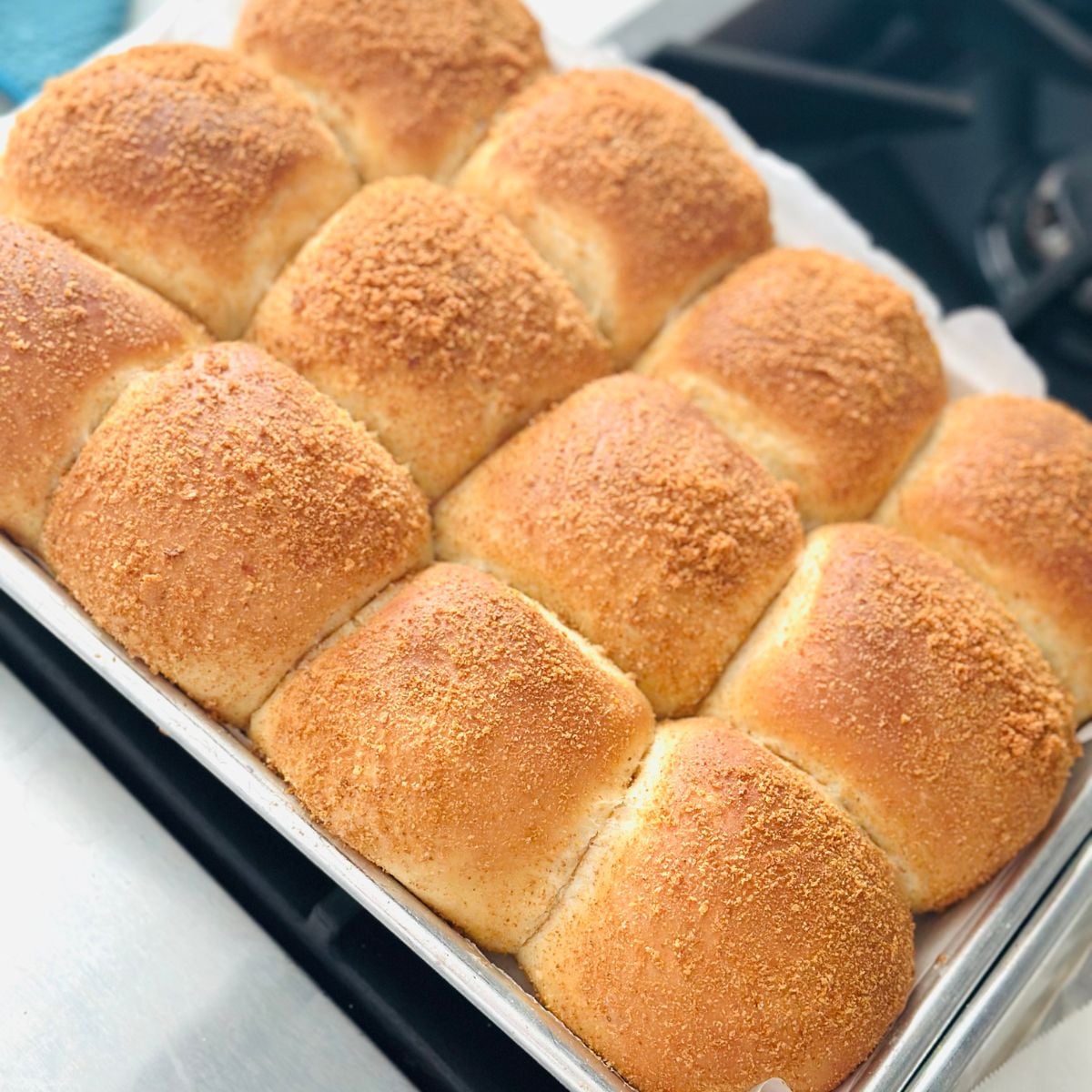 Freshly baked pandesal rolls in a baking pan with golden brown tops and breadcrumb coating.