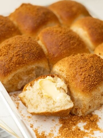 Close-up of baked pandesal with one roll opened to show the soft, fluffy interior with butter inside.
