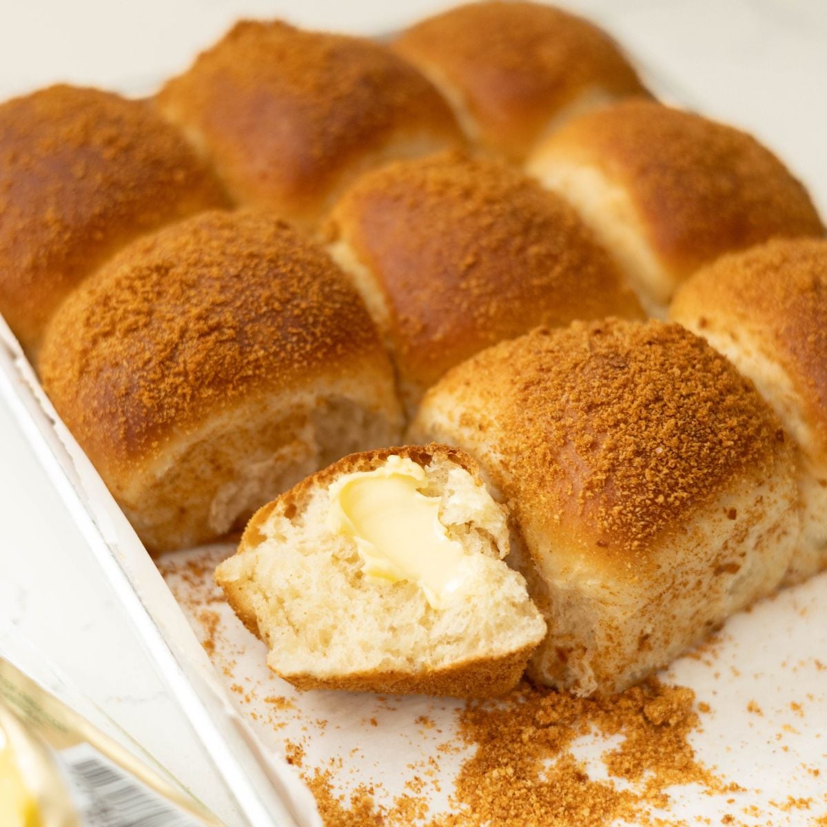 Close-up of baked pandesal with one roll opened to show the soft, fluffy interior with butter inside.