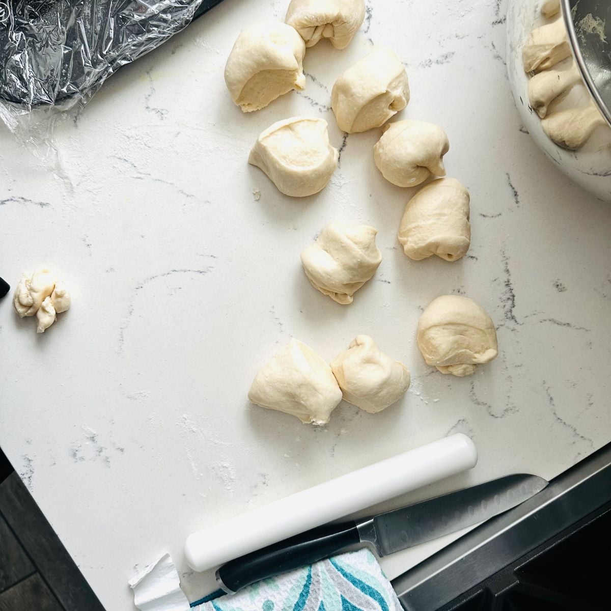 Divided portions of soft bread dough on a lightly floured countertop beside a rolling pin and knife.