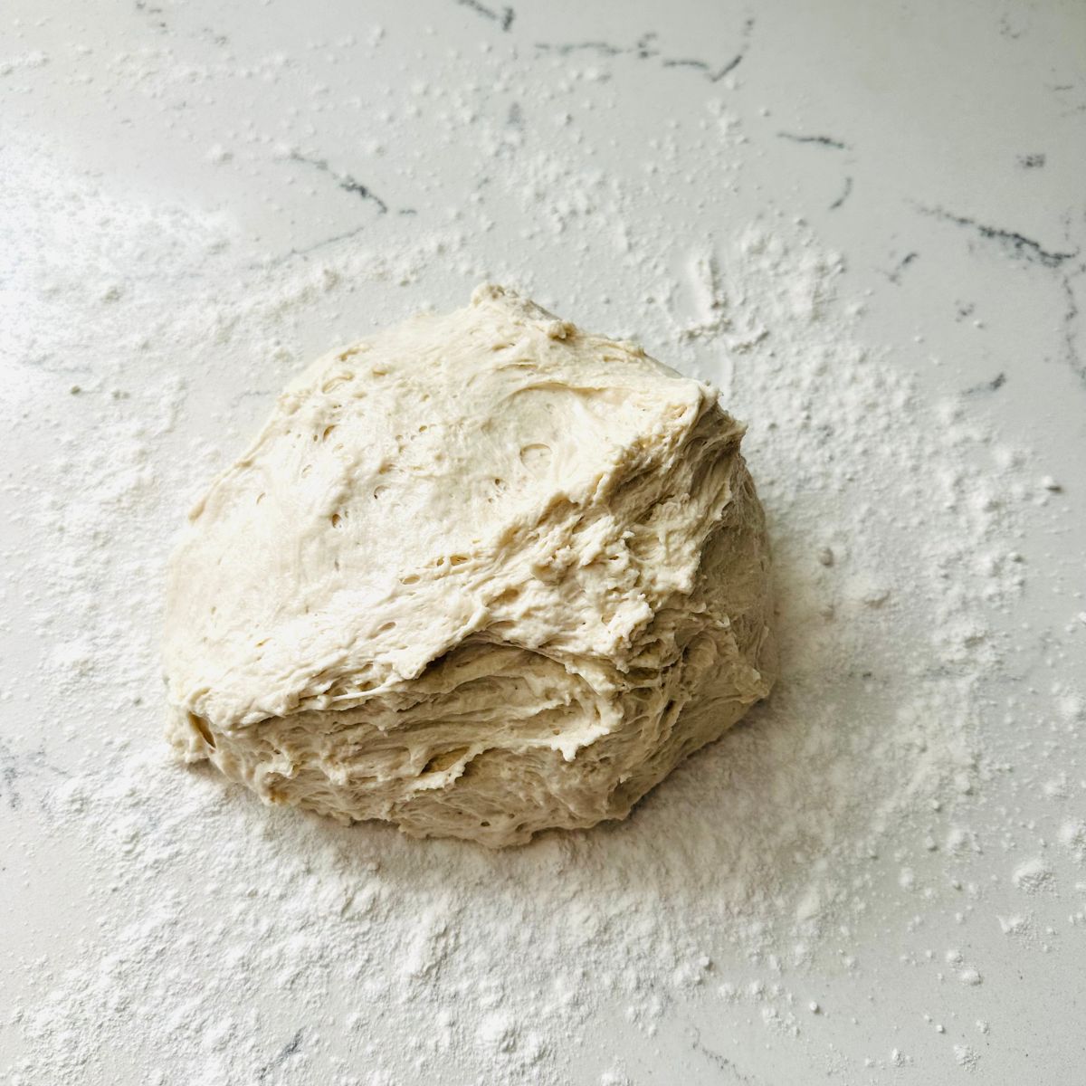 Sticky bread dough placed on a floured countertop, ready for kneading or shaping.