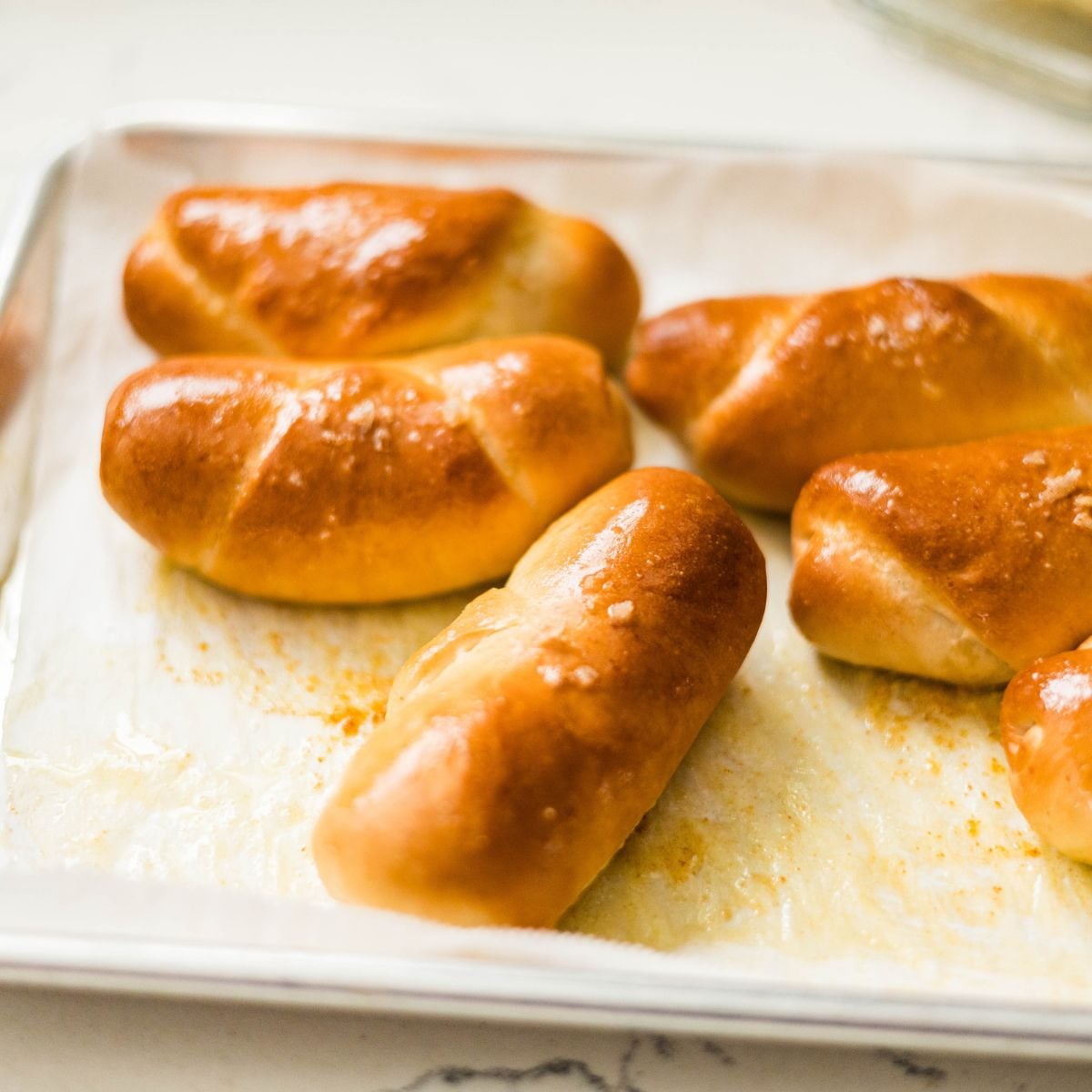 Freshly baked shio pan rolls on a baking sheet, golden brown and glossy from melted butter.