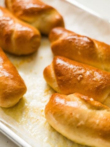 Close-up of baked salt bread rolls with deep golden tops and buttery shine on a parchment-lined pan.