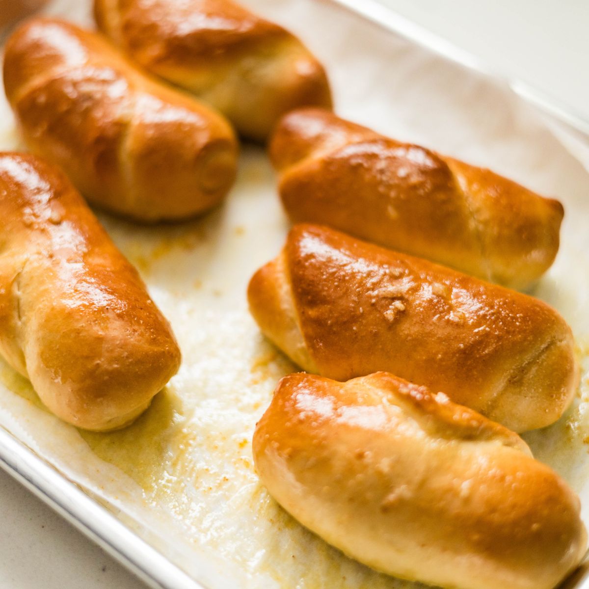 Close-up of baked salt bread rolls with deep golden tops and buttery shine on a parchment-lined pan.