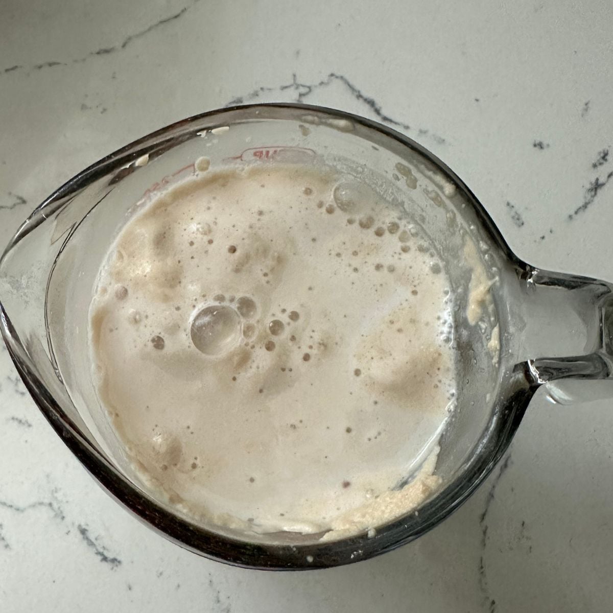 Yeast mixture with milk bubbling in a glass measuring cup, ready to be added to the dough.
