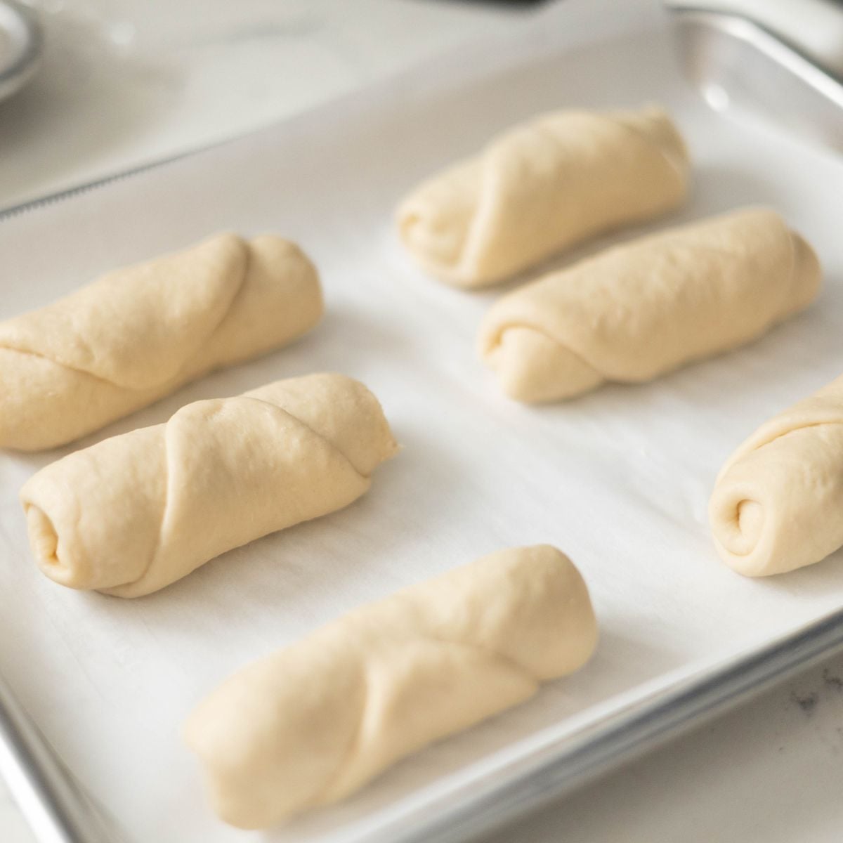 Shaped shio pan rolls arranged on a parchment-lined baking sheet, ready for proofing or baking.