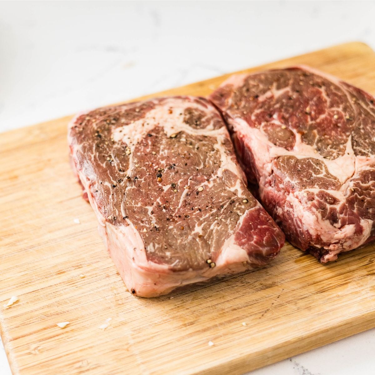Raw ribeye steaks seasoned with black pepper on a wooden cutting board for beef salpicao.