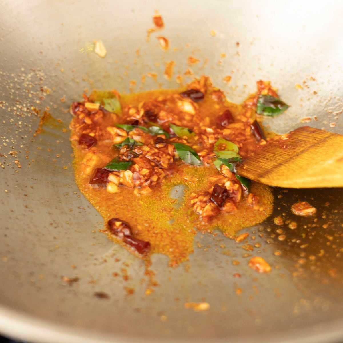 Garlic, ginger, dried chilies, curry leaves, and Kashmiri chili powder cooking in a wok