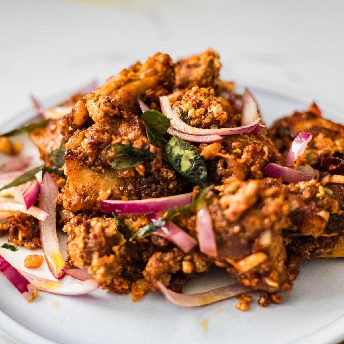 Chicken 65 served on a plate with red onions, curry leaves, and crispy fried coating