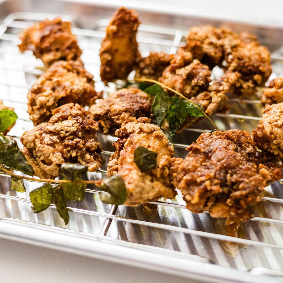 Crispy fried Chicken 65 pieces draining on a wire rack with fried curry leaves