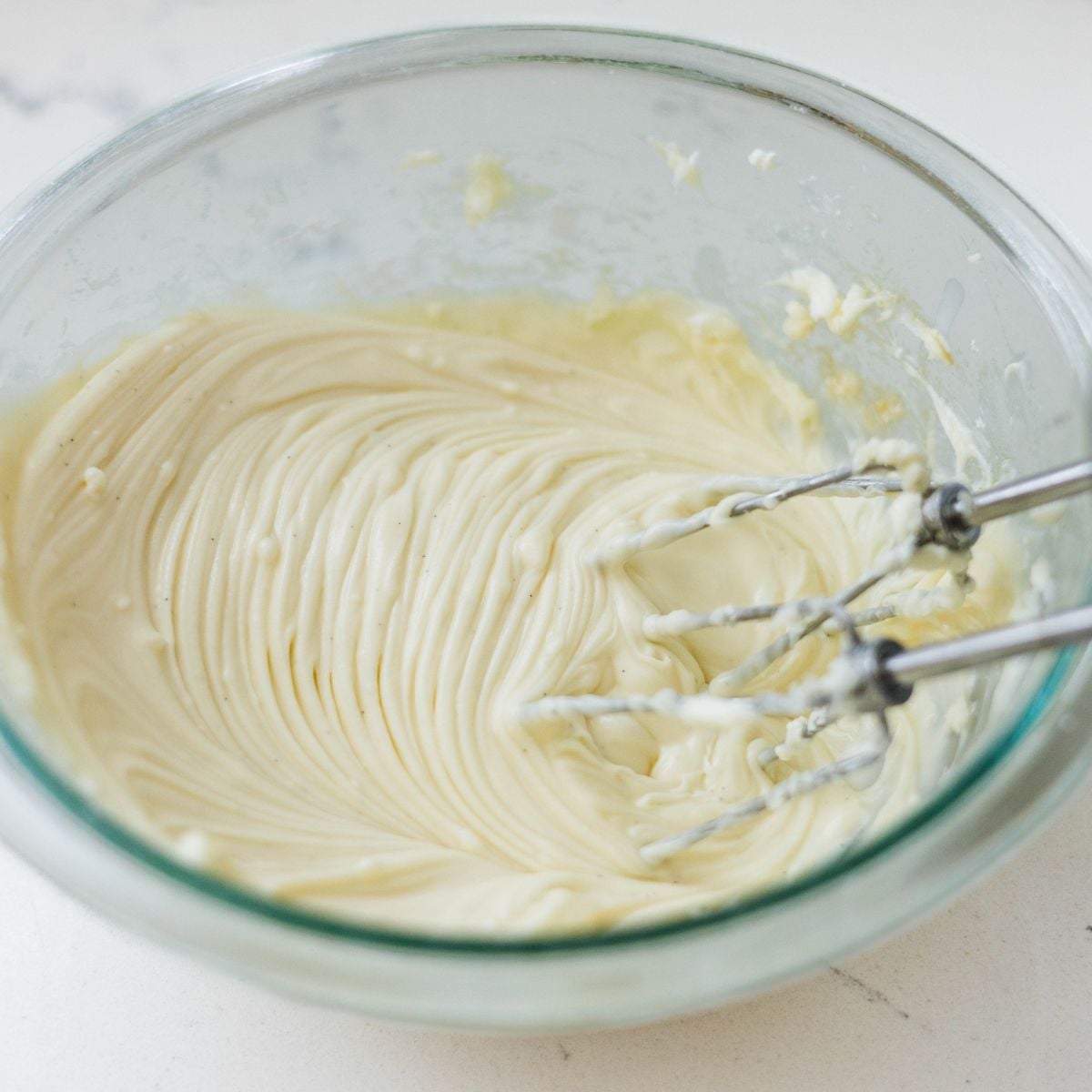 Smooth cinnamon roll cream cheese frosting being mixed in a glass bowl with hand mixer