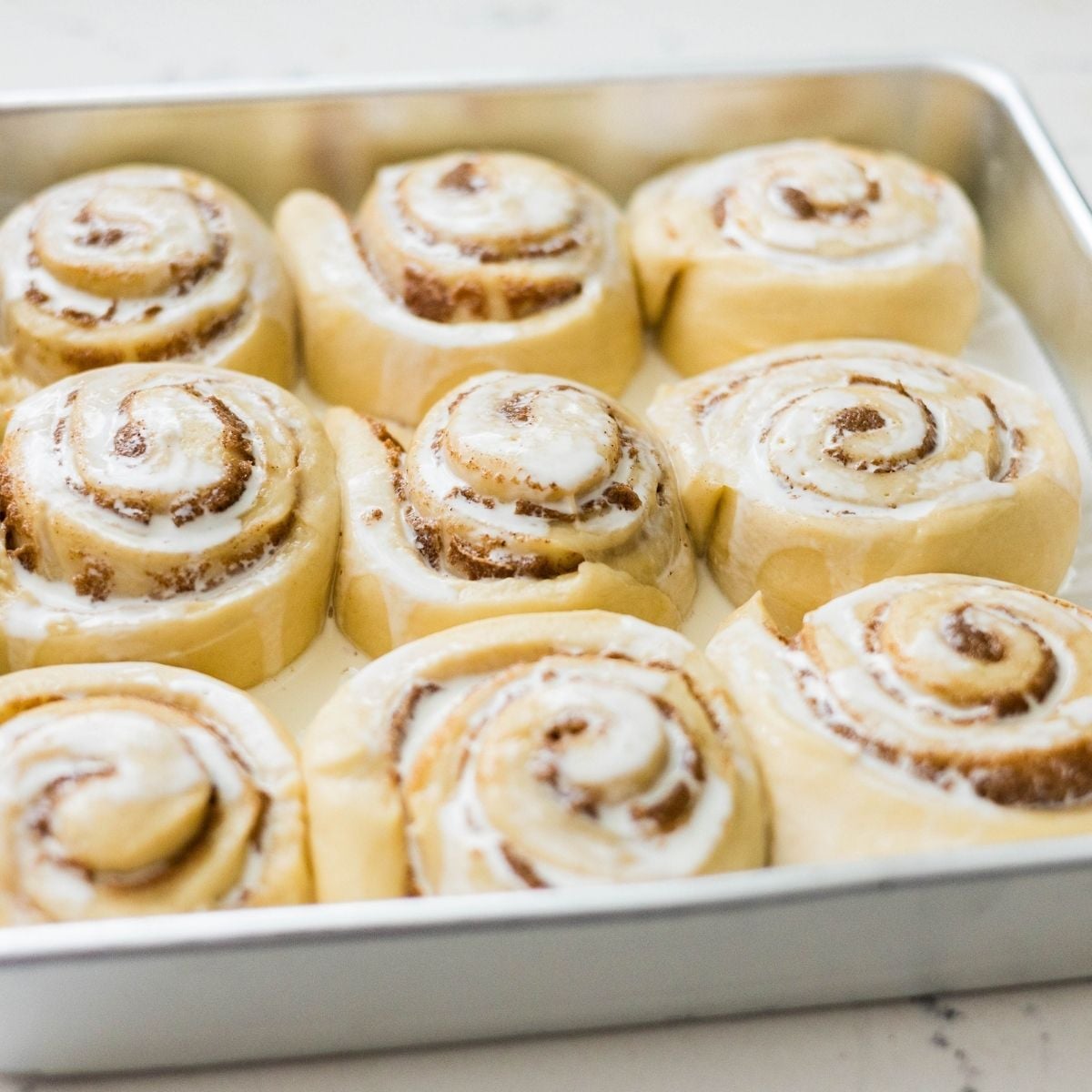 Classic cinnamon rolls in a baking pan topped with heavy cream before baking