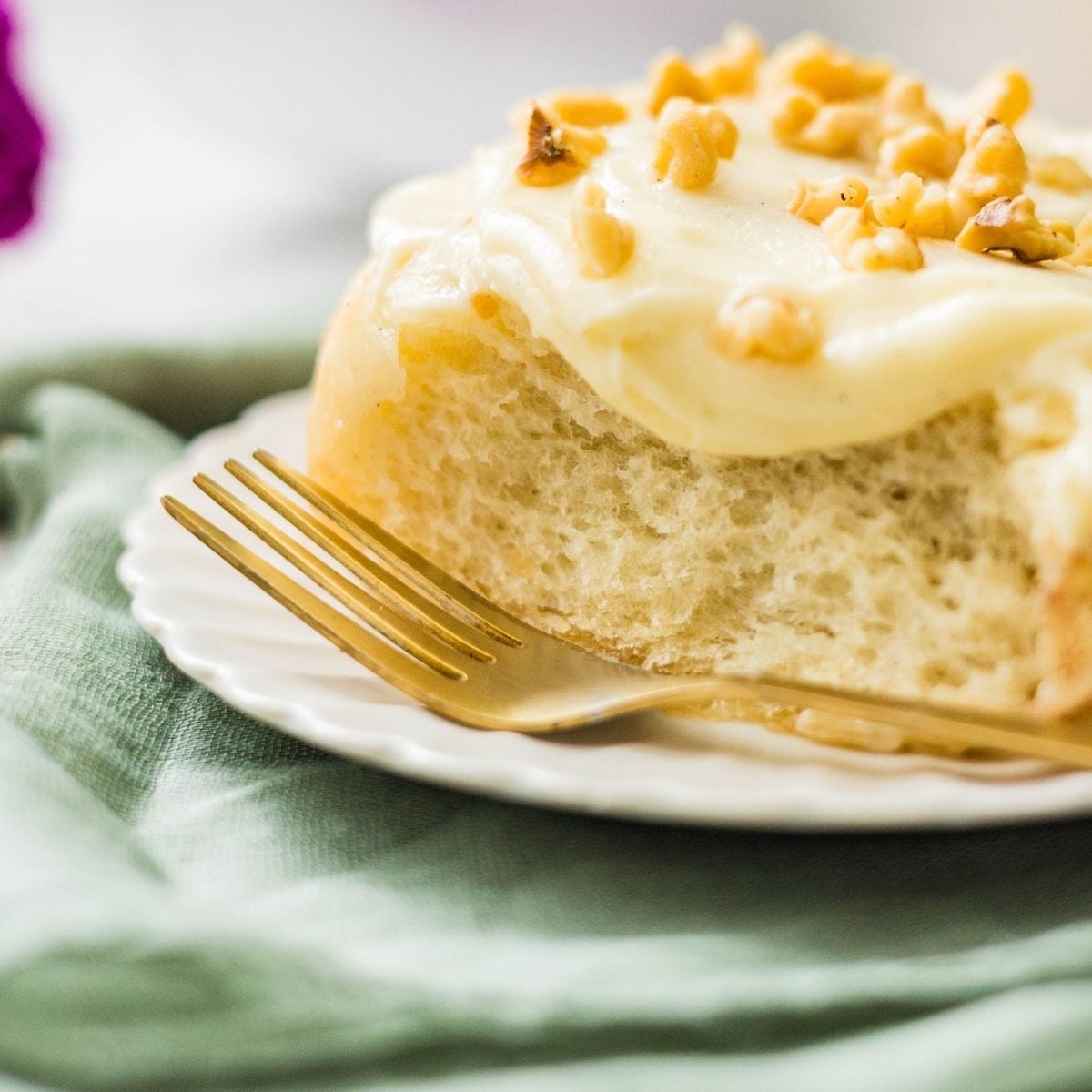 Close-up of a cinnamon roll topped with cream cheese frosting and chopped walnuts on a plate