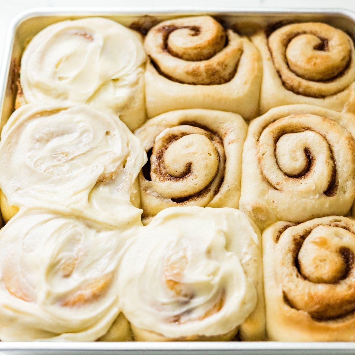 Classic cinnamon rolls in a pan with thick cream cheese frosting spread over the tops