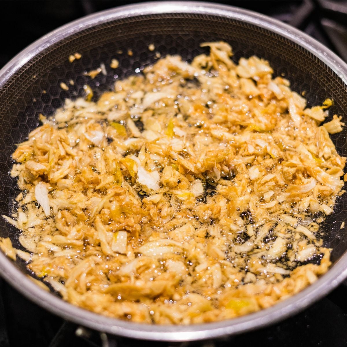 Crispy golden fried garlic cooking in oil in a pan for Filipino garlic fried rice sinangag.