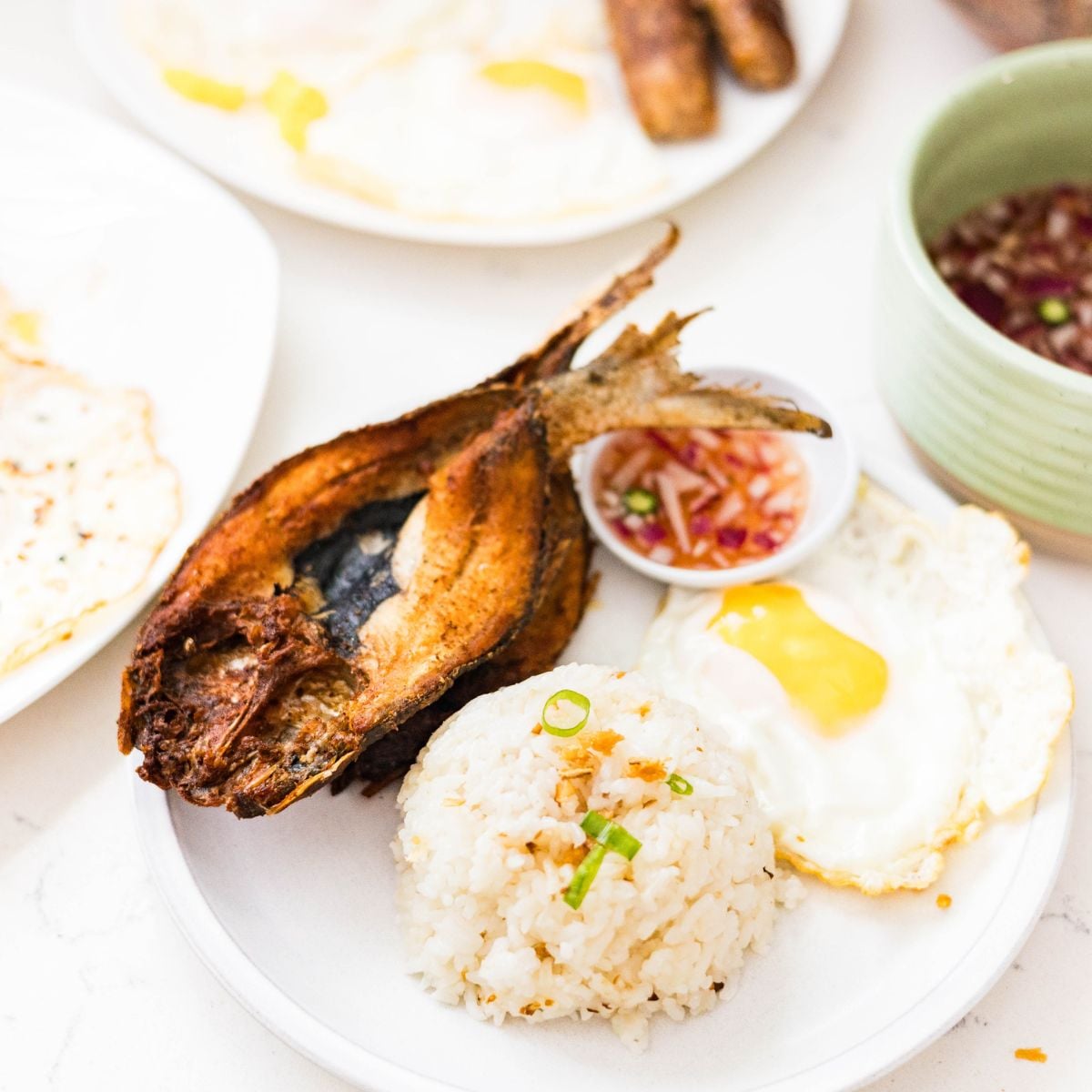 Filipino breakfast plate with garlic fried rice, fried egg, daing na bangus, and dipping sauce.
