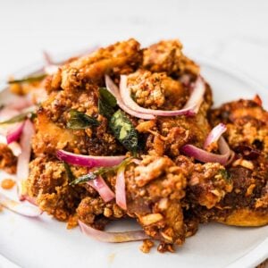 Chicken 65 served on a plate with red onions, curry leaves, and crispy fried coating