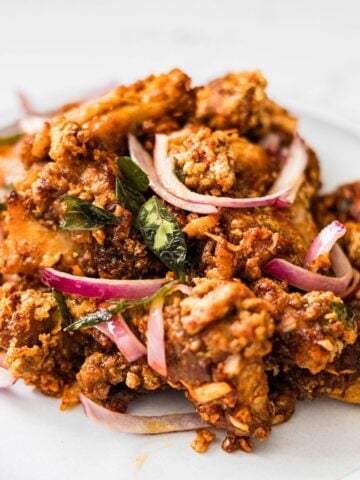 Chicken 65 served on a plate with red onions, curry leaves, and crispy fried coating
