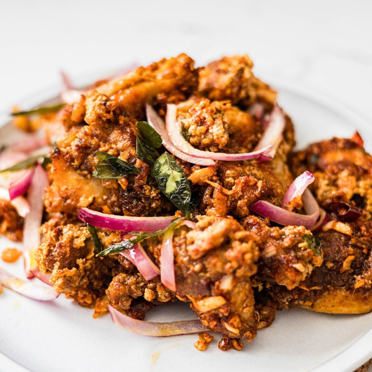 Chicken 65 served on a plate with red onions, curry leaves, and crispy fried coating
