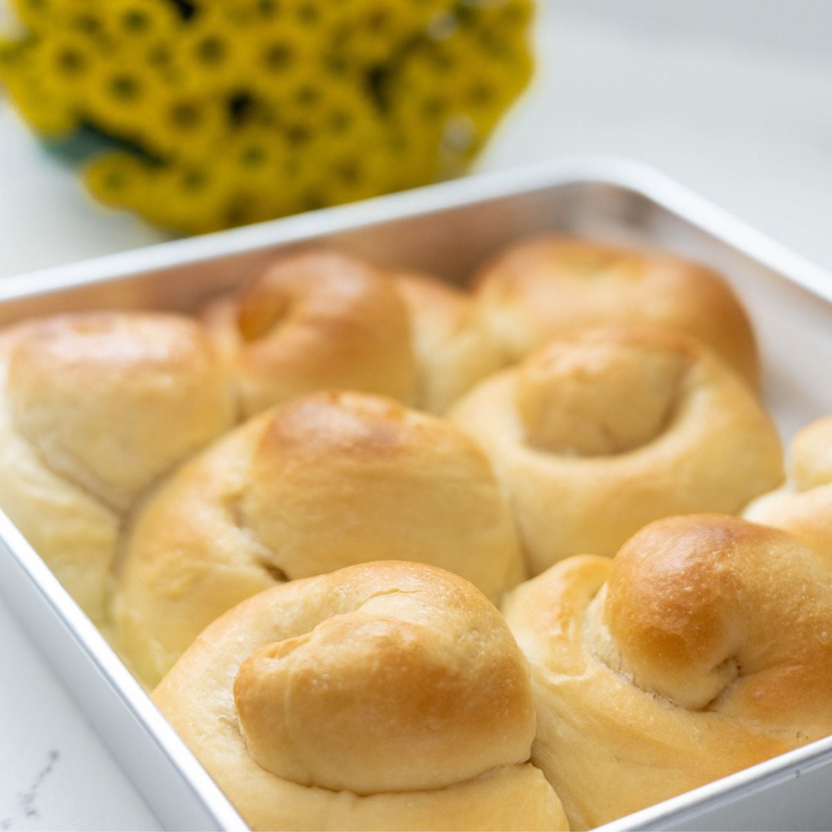Freshly baked Filipino ensaymada rolls in a square pan before frosting