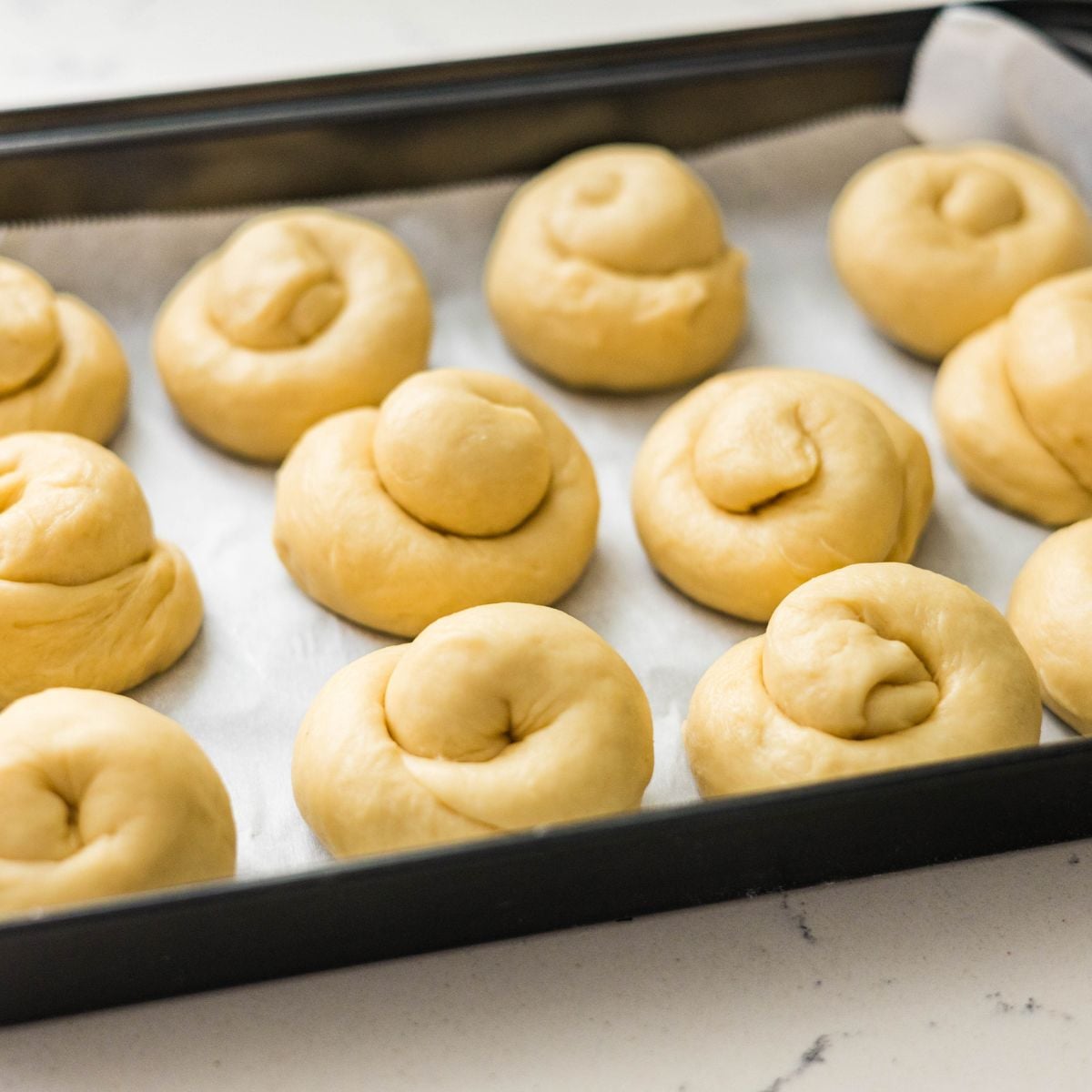 Coiled Filipino ensaymada dough proofing on a lined baking sheet before baking