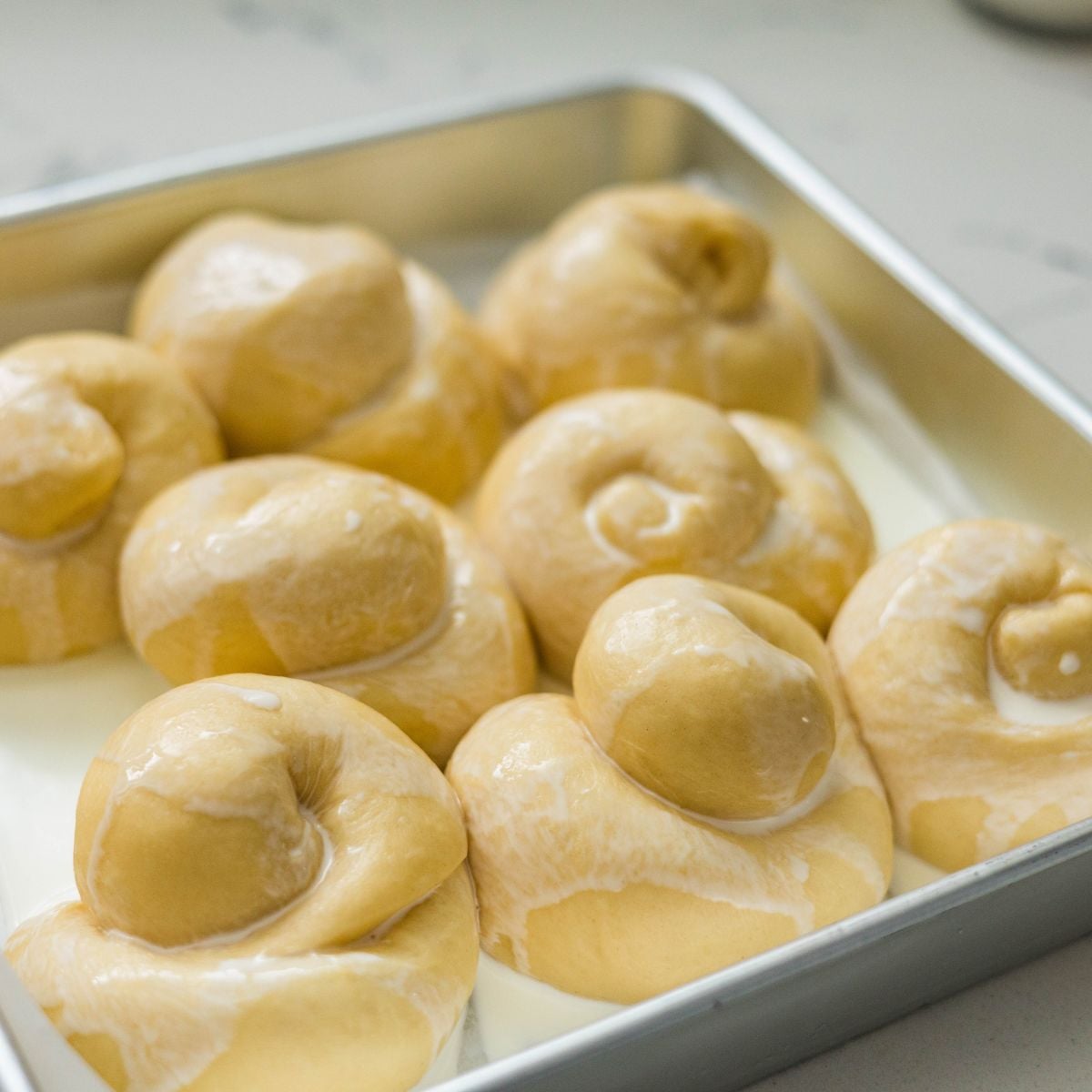 Filipino ensaymada rolls drizzled with heavy cream before baking