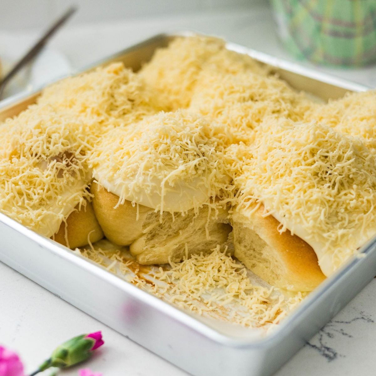 Single Filipino ensaymada topped with cream cheese frosting and grated cheese on a plate