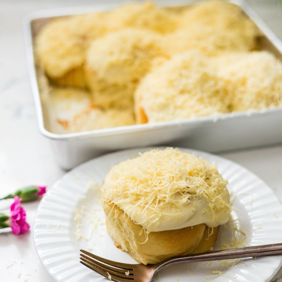 Pan of Filipino ensaymada topped with generous cream cheese frosting and shredded cheese