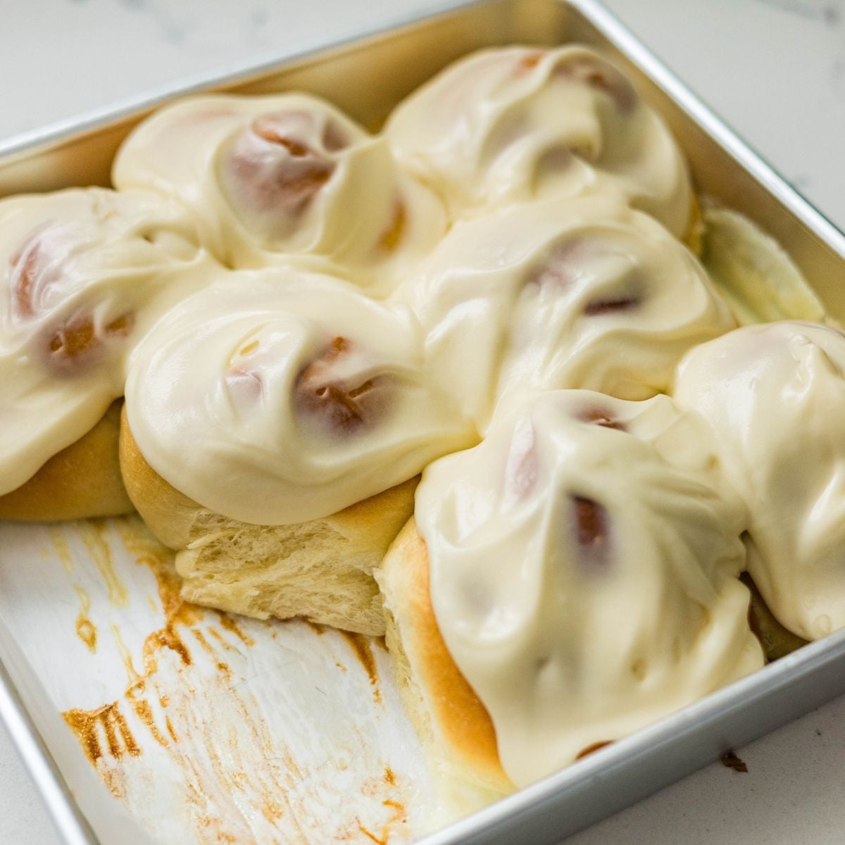 Close-up of Filipino ensaymada rolls with smooth cream cheese frosting in a baking pan