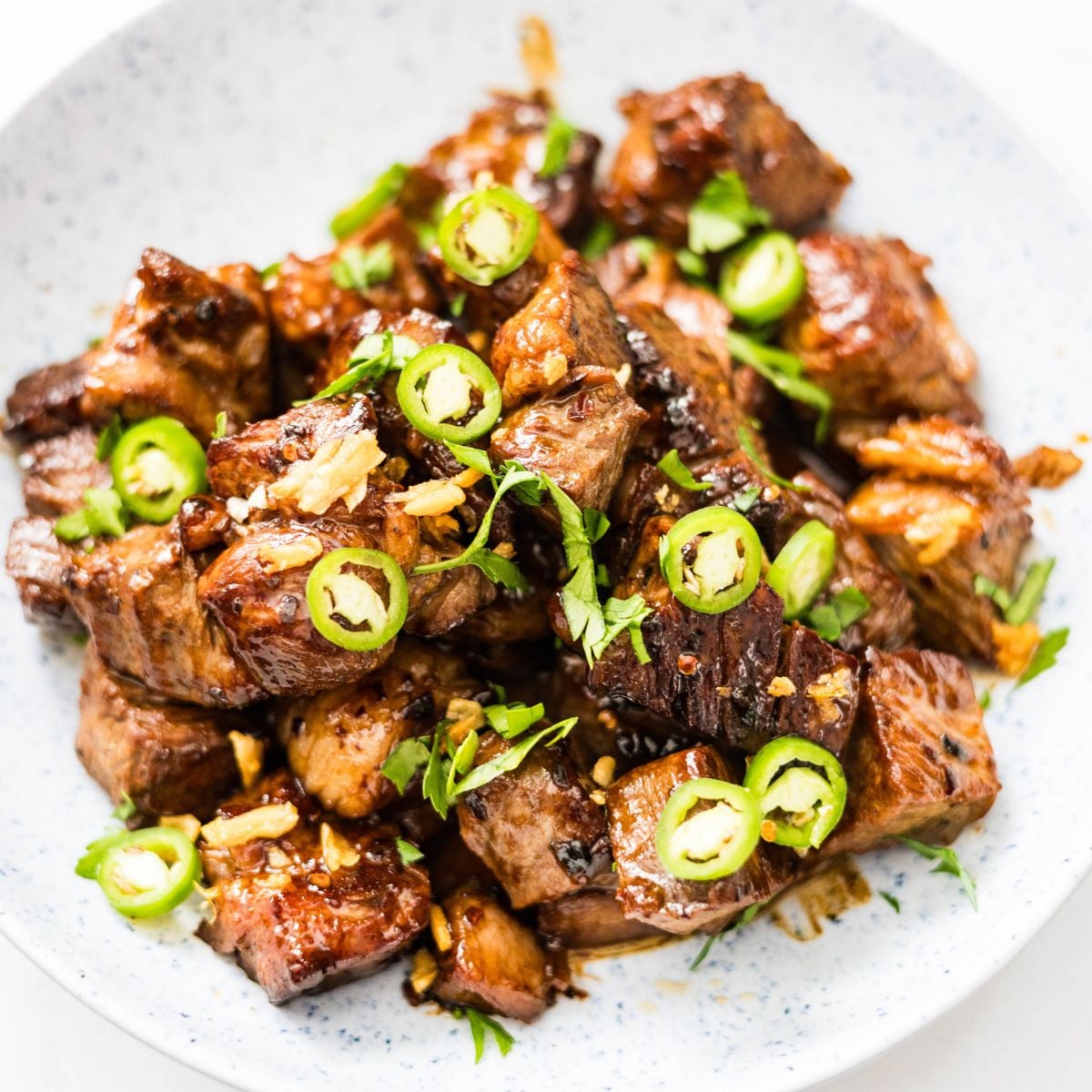 Filipino beef salpicao served with sliced green chilies, crispy garlic, and fresh herbs.