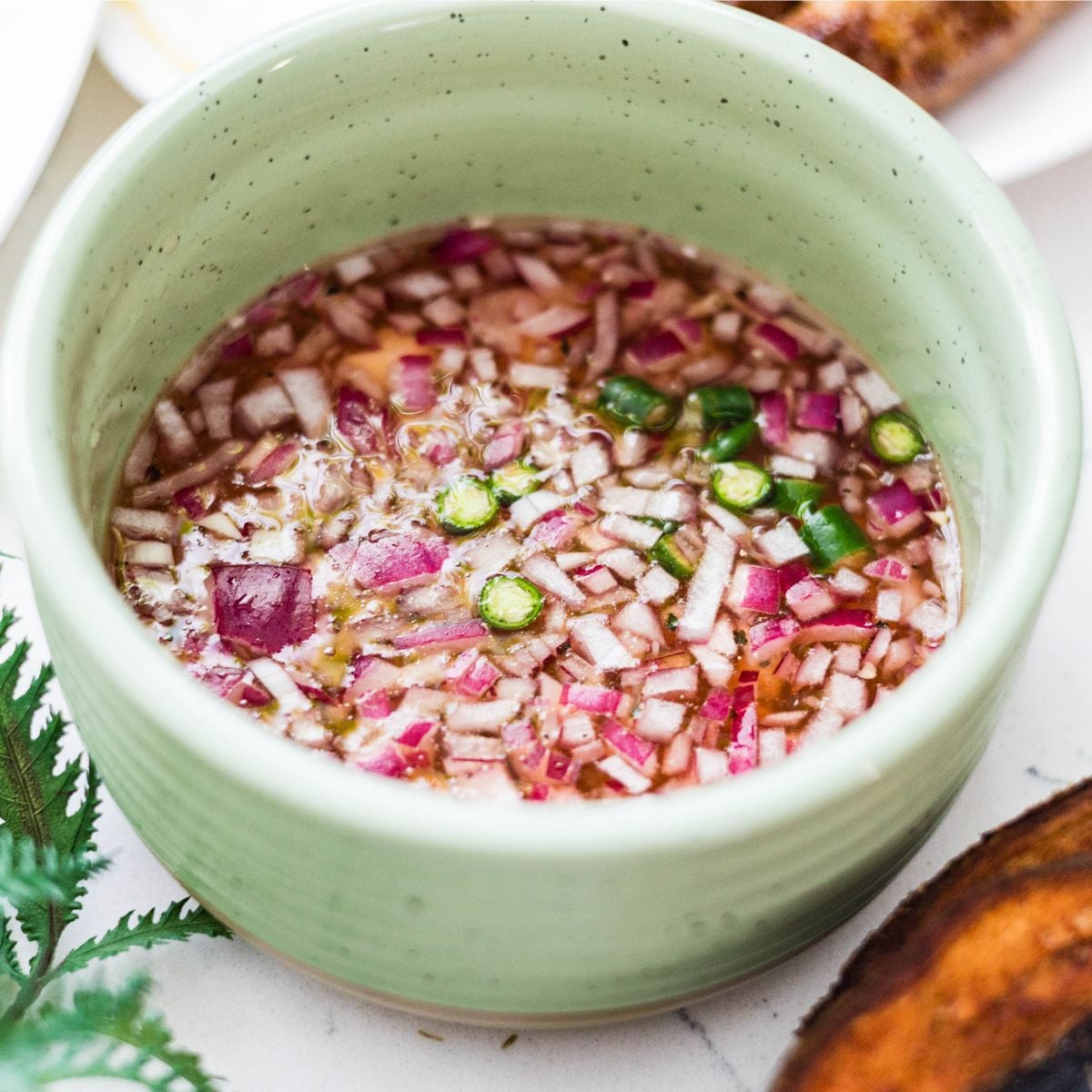 Filipino sawsawan dipping sauce with vinegar, red onion, and green chili in a bowl.