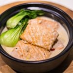 Ginataang salmon in a clay pot with bok choy, red chili, and rich coconut milk sauce