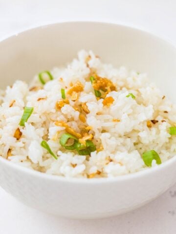 Bowl of Filipino garlic fried rice sinangag topped with crispy garlic and green onions.