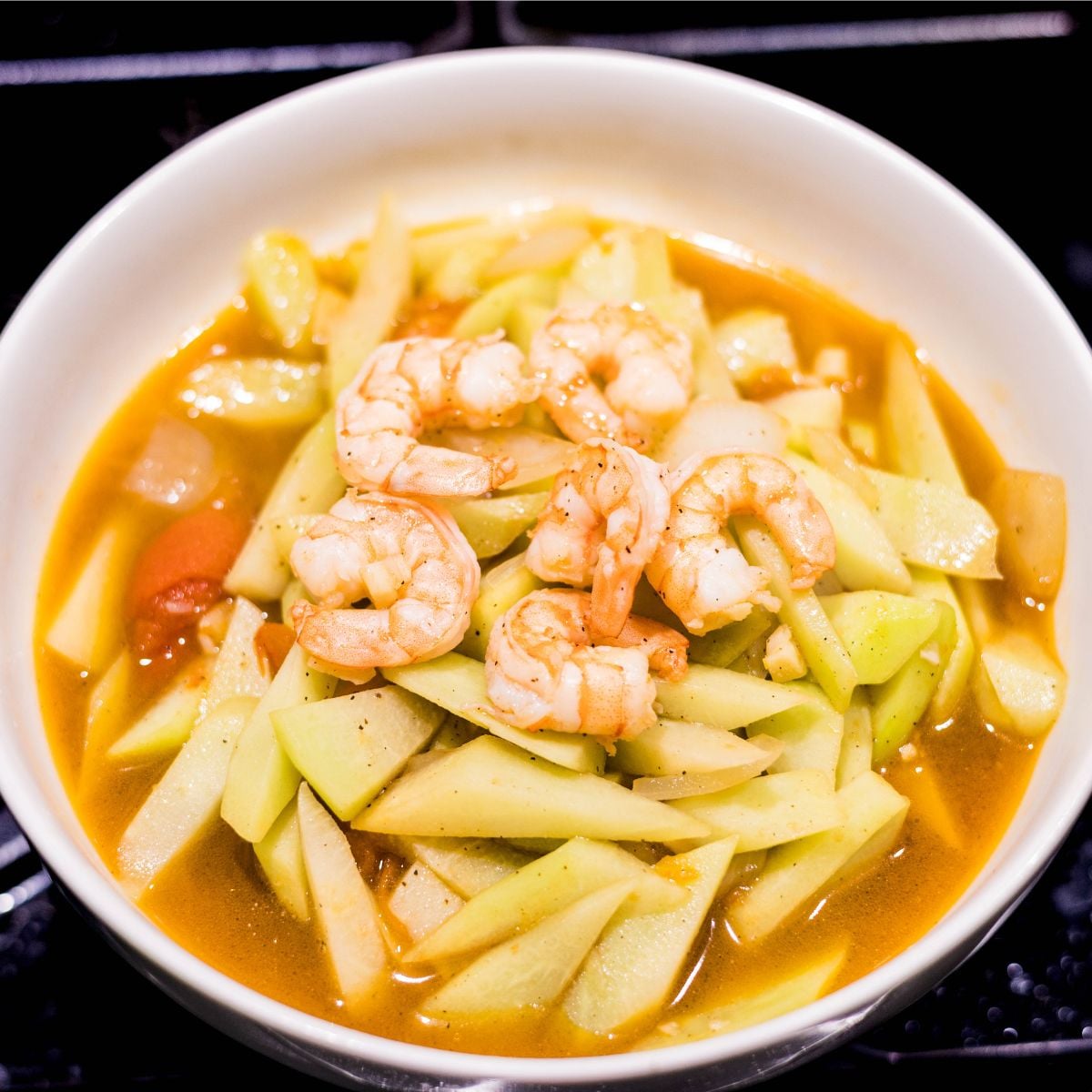 Close-up of ginisang sayote with shrimp, tomatoes, and onion in a light broth.