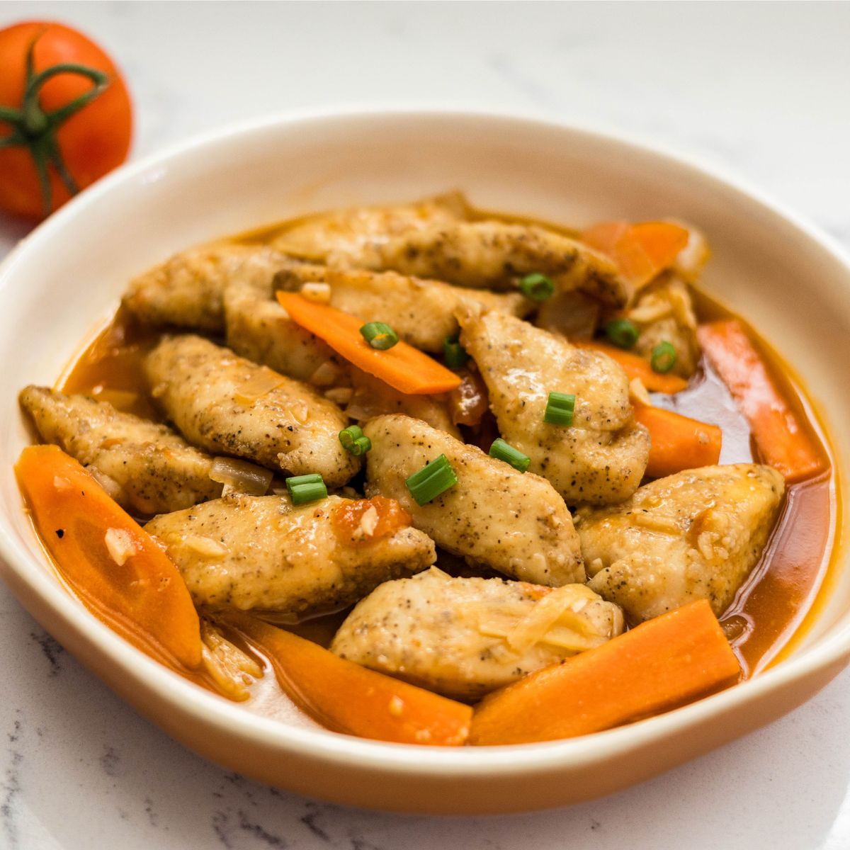 Hoisin fish served in a shallow bowl with carrots and sauce, topped with chopped green onions.