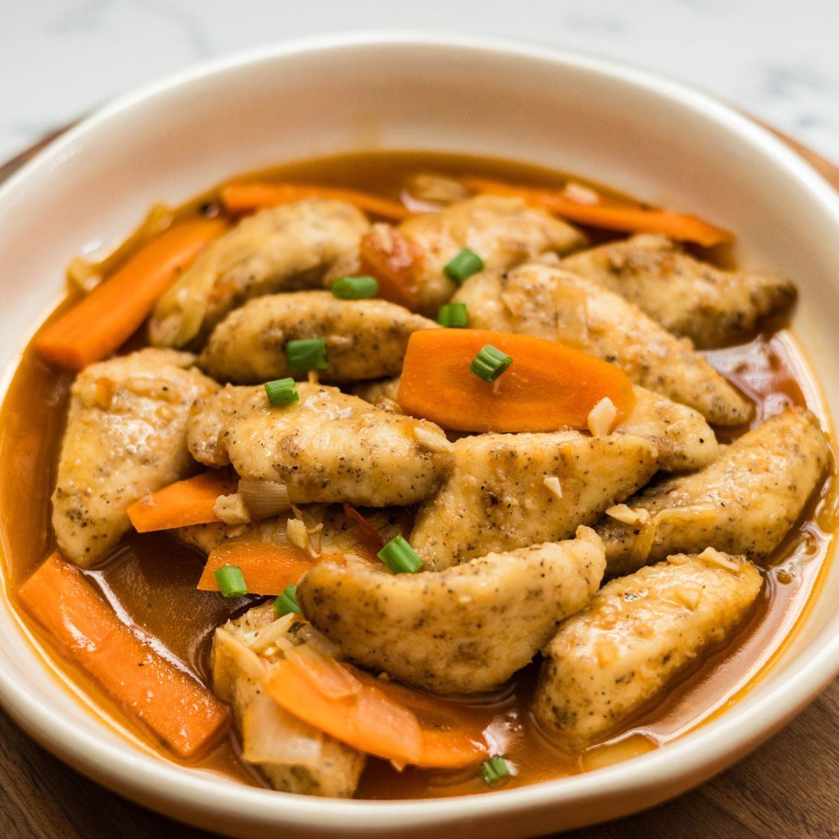 Close-up of hoisin fish with carrot slices in a savory sauce.