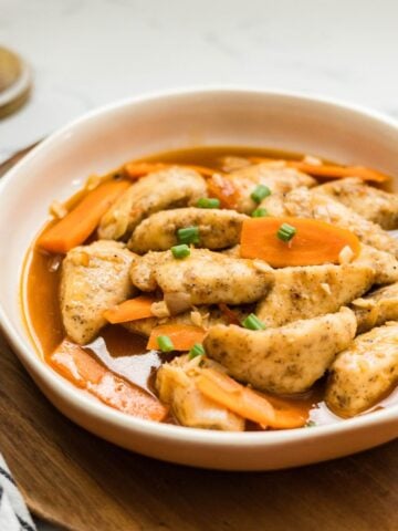 Hoisin fish plated in a shallow bowl on a wooden board.