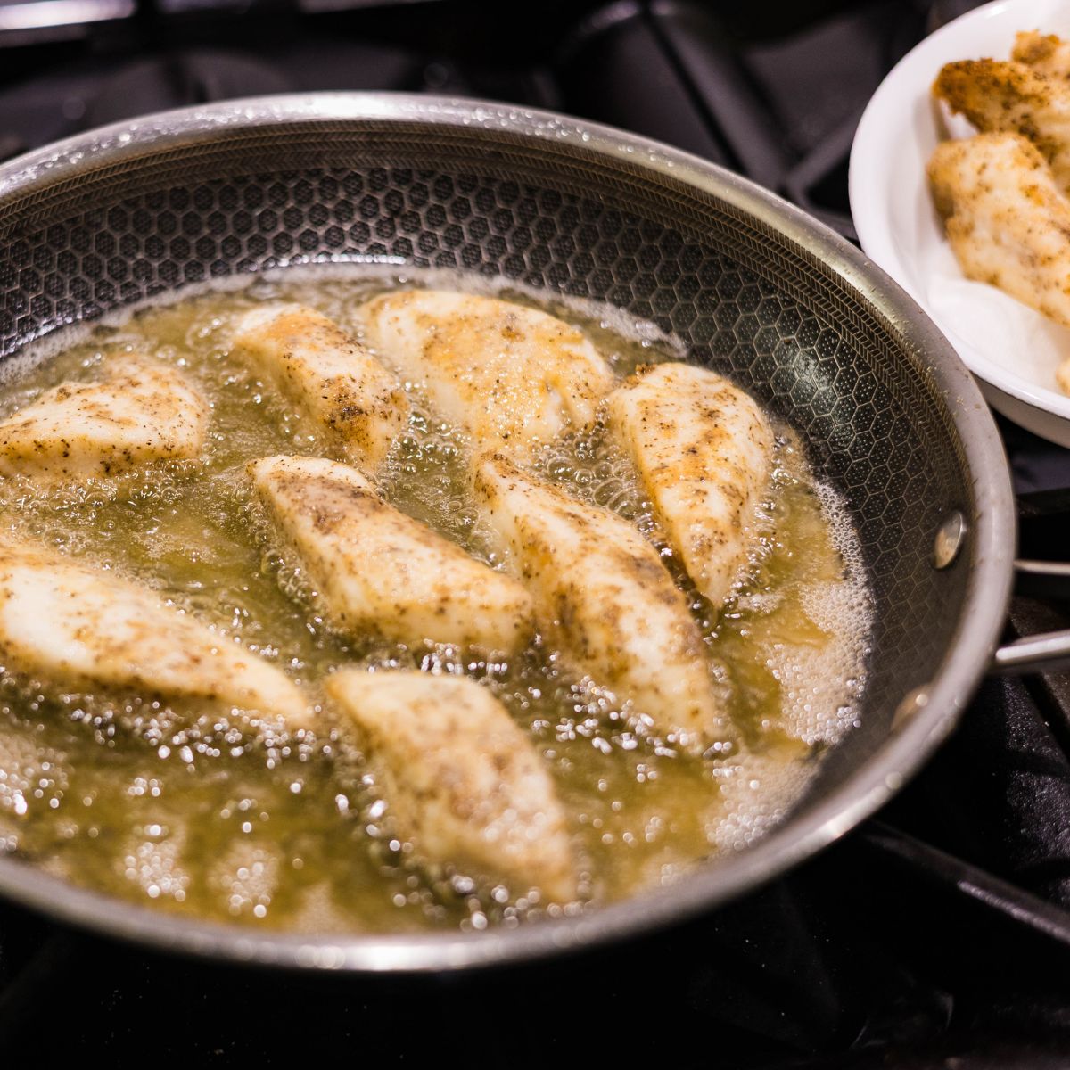 Tilapia fillets frying in oil in a skillet until golden.