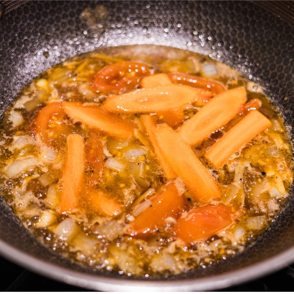 Carrot slices simmering in a hoisin sauce mixture with onions and tomatoes in a skillet.