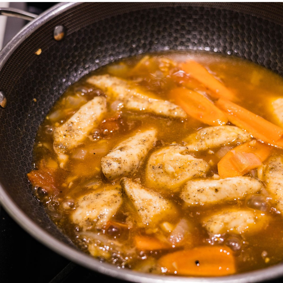 Seasoned fish fillets simmering in hoisin sauce with carrots in a skillet.