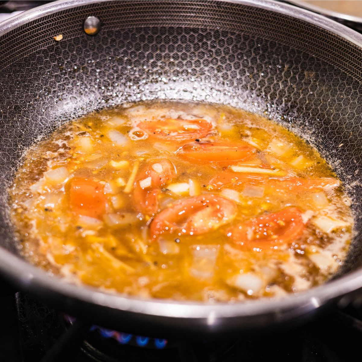 Tomatoes and onions simmering in a glossy hoisin sauce in a skillet.